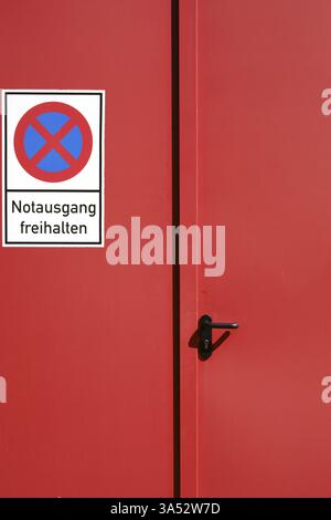 A bright red painted emergency exit consisting of a steel door with a sign Stock Photo
