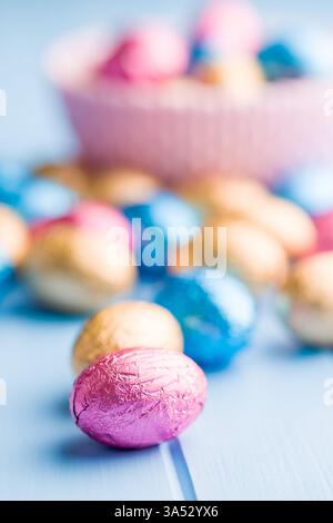 Chocolate easter eggs wrapped in multi colored foil on a blue table. Stock Photo