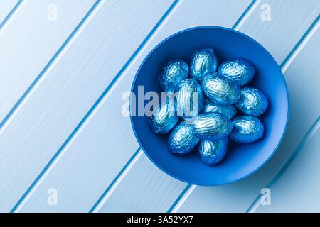 Chocolate easter eggs wrapped in blue colored foil on a blue table. Stock Photo