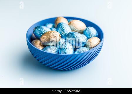 Chocolate easter eggs wrapped in multi colored foil on a blue background. Stock Photo