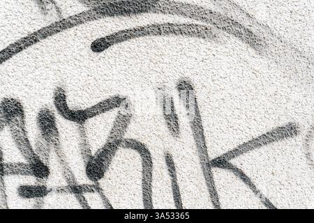 Black graffiti lettering adorns a textured white wall in an urban area, showcasing artistic expression through abstract designs and bold strokes. The Stock Photo