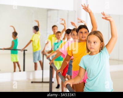 Focused tween girl practicing ballet positions near bar during group class Stock Photo