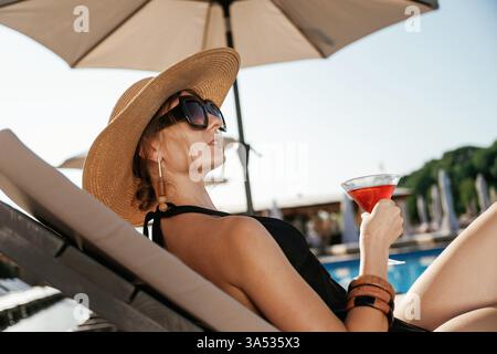 Side view, lying down with cocktail in hand. Beautiful young woman is at resort, vacation. Stock Photo