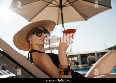 Side view, lying down with cocktail in hand. Beautiful young woman is at resort, vacation. Stock Photo