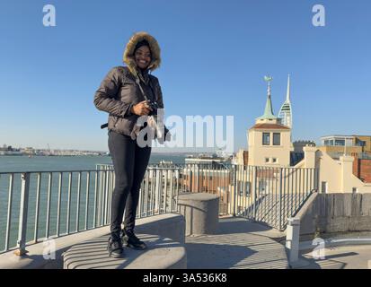 Portsmouth England UK. 18.03.2025. Woman with fur lined hood taking pictures during winter Portsmouth Harbour, Stock Photo