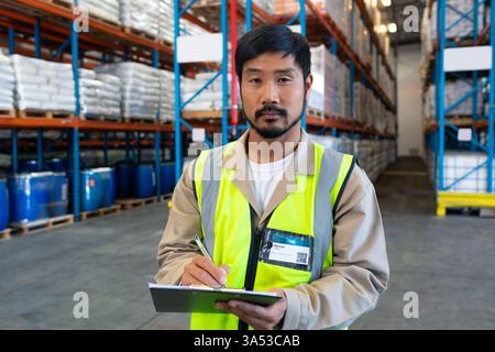Warehouse worker in safety vest checking inventory on clipboard, ensuring accuracy Stock Photo