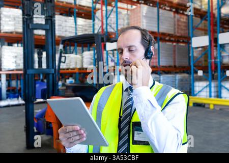 Using tablet and headset, warehouse manager managing inventory and communicating Stock Photo