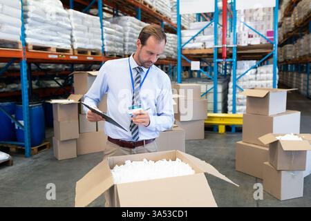 In warehouse, manager checking inventory with clipboard among stacked boxes, copy space Stock Photo