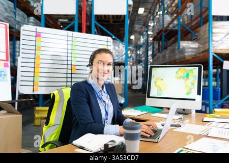 Using computer and headset, warehouse manager coordinating logistics efficiently, copy space Stock Photo