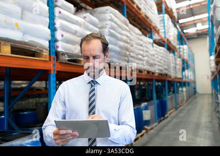 Businessman using tablet in warehouse, checking inventory on storage shelves Stock Photo