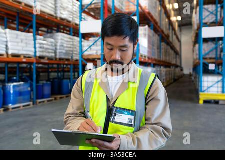 In warehouse, worker in high-visibility vest checking inventory using clipboard Stock Photo