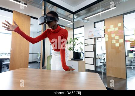 Woman using VR headset in modern office, interacting with virtual environment Stock Photo