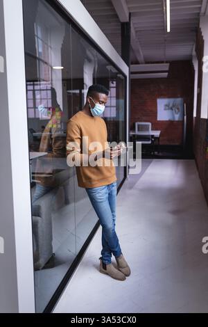 African American man using tablet in modern office, wearing protective face mask Stock Photo