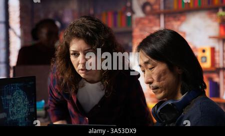 IT engineers cooperating in AI focused startup, debugging applications, crosschecking between PC and laptop. Coworkers doing code testing and quality assurance on devices, camera B close up Stock Photo