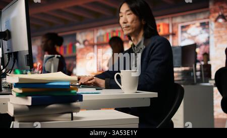 Senior engineer coding advanced AI algorithm in startup office, refining machine learning models to enhance automation. Asian CTO manager using coding platform in Silicon Valley workplace, camera A Stock Photo