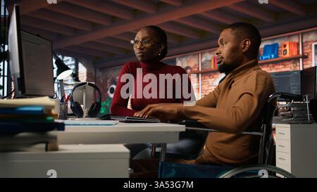 Manager coming to inclusive startup office employee in wheelchair desk to offer help. Thoughtful supervisor checking up on software development agency worker with disability, camera A Stock Photo