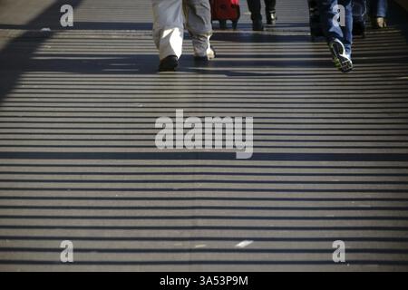 A bridge railing casts striped symmetrical shadows on a pavement Stock Photo