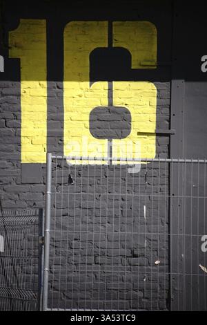 A large yellow building number painted on a striking dark grey brick wall Stock Photo