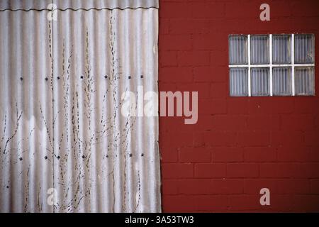 A close-up of a window made of glass tiles on a red-painted wall with adjoining corrugated sheet metal Stock Photo