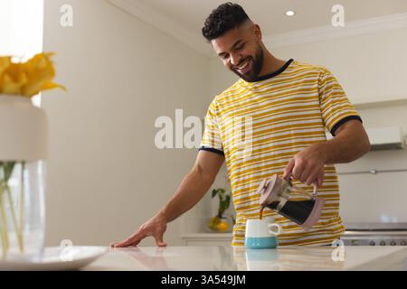 Smiling man in striped shirt pouring coffee in kitchen, enjoying morning routine, copy space Stock Photo