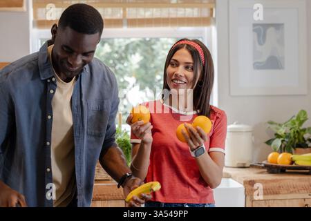 Smiling Diverse couple in kitchen preparing fresh fruit, enjoying time together Stock Photo