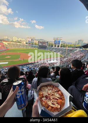 A person enjoying pizza and beer while watching a professional baseball game in a crowded stadium during the evening. Stock Photo