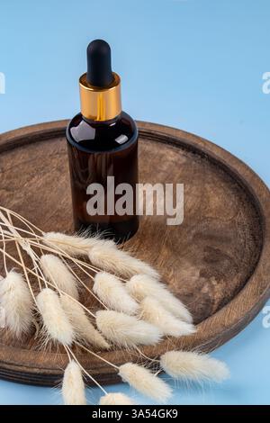 Amber glass dropper bottle with beauty care serum, hyaluronic acid and vitamins on wooden tray on blue background decorated trendy lagurus reed grass. Stock Photo
