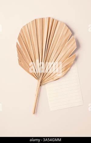 Blank card on dry beige palm leaf top view, mockup. Boho scene. close to nature greeting or wedding vertical Invitation. Minimal composition Stock Photo