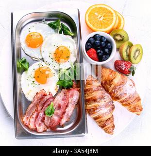 Table set for traditional breakfast with eggs, bacon, croissants and berries on a white background.. Top view Stock Photo