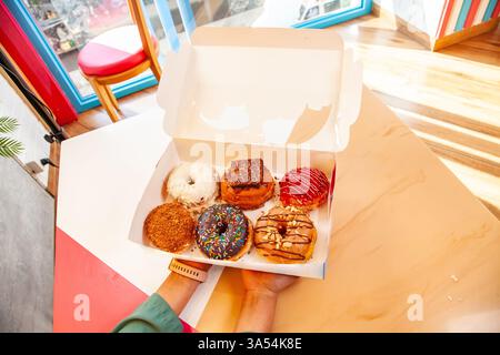 Hand holding doughnut box of assorted mixed hand made brioche donuts. Stock Photo