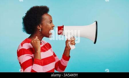 Black woman, loudspeaker and power for protest in studio with opinion, fist and anger by blue background. Person, college student and shout on Stock Photo