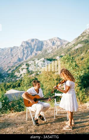 Montenegro, Bar - July 09, 2024: Violinist plays the violin while standing next to a seated guitarist playing the guitar in the mountains Stock Photo