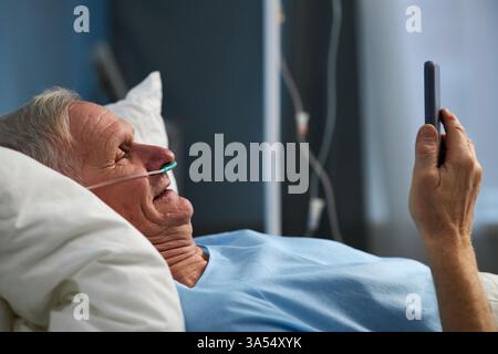 Elderly Man Using Smartphone While Lying in Bed Stock Photo