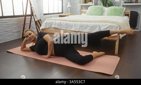 Woman exercising on a yoga mat in a modern bedroom with wooden flooring and large windows, showcasing healthy lifestyle indoors. Stock Photo