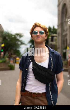 man with red hair wearing sunglasses strolls through an urban area Stock Photo