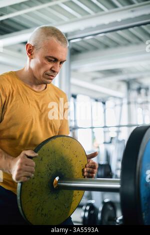 Senior Man Loading Weight Plates onto a Barbell in a Gym Stock Photo