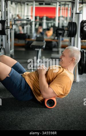 Man doing back muscle recovery exercises with a foam roller in the gym Stock Photo