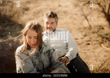 A couple relaxes on a rock, soaking in the golden light Stock Photo