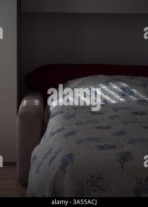 Sunlit Shutter Patterns Cast on a Bed with Coastal Print Blanket Stock Photo