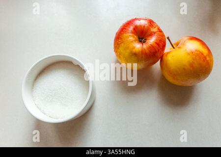 White sugar in a sugar bowl and two washed apples on the table Stock Photo