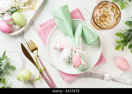 Easter table setting on white background with spring decorations. White plate, cutlery and colored eggs. Flat lay. Stock Photo