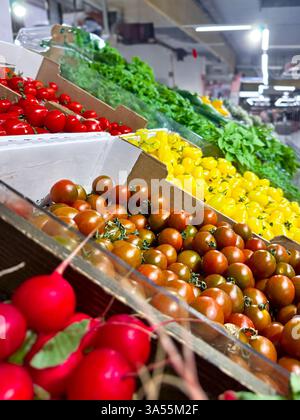 Various type of fresh fruits arrange neatly, grocery store. Radishes, tomatoes, yellow peppers, green vegetables on rack.  Stock Photo