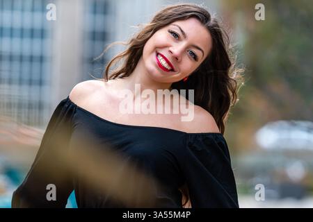 A woman with long hair and red lips poses confidently in an outdoor area. Stock Photo