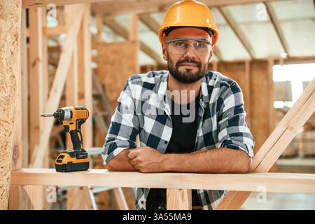 Leaning on the unfinished wooden house, building. Industrial worker in warehouse. Stock Photo
