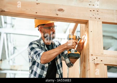 Busy, drilling the hole. Industrial worker in wooden warehouse. Stock Photo
