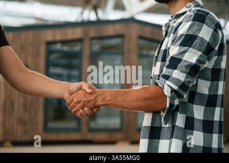 Close up view, doing handshake. Two workers are in the industrial wooden warehouse. Stock Photo