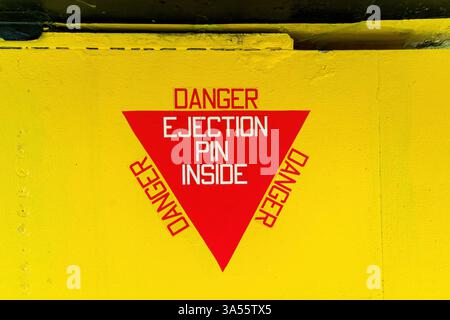 Red triangular warning sign displaying the words danger ejection pin inside on a light blue industrial surface Stock Photo
