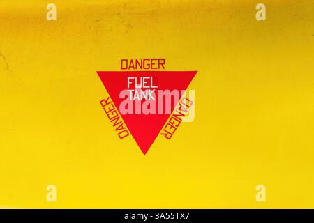 Red triangular warning sign displaying the words danger fuel tank on a yellow painted jet aircraft Stock Photo