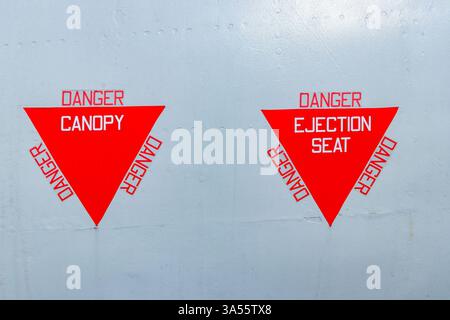 Red triangular warning sign displaying the words danger canopy & ejection seat on a silver painted military jet aircraft Stock Photo