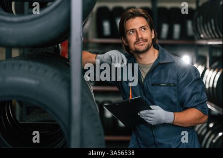 Holding black notepad. Man is in the tire fitting car service. Stock Photo